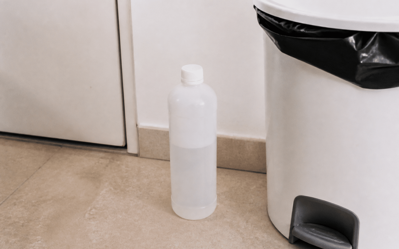 Bouteille plastique acetone posee verticalement pres poubelle recyclage