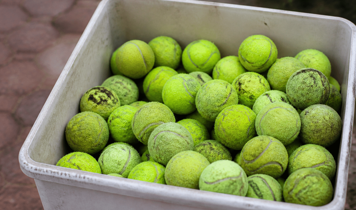 Balles de tennis jaunes usagees empilees dans un bac de collecte