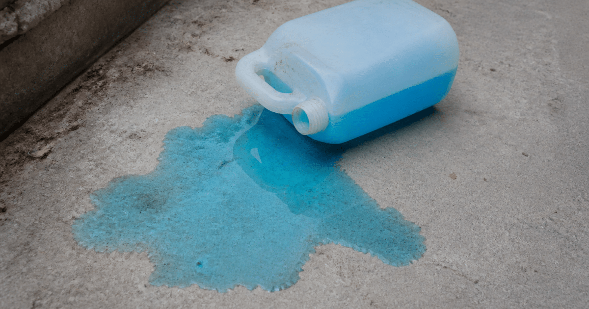 Bidon antigel bleu renverse sur sol beton gris