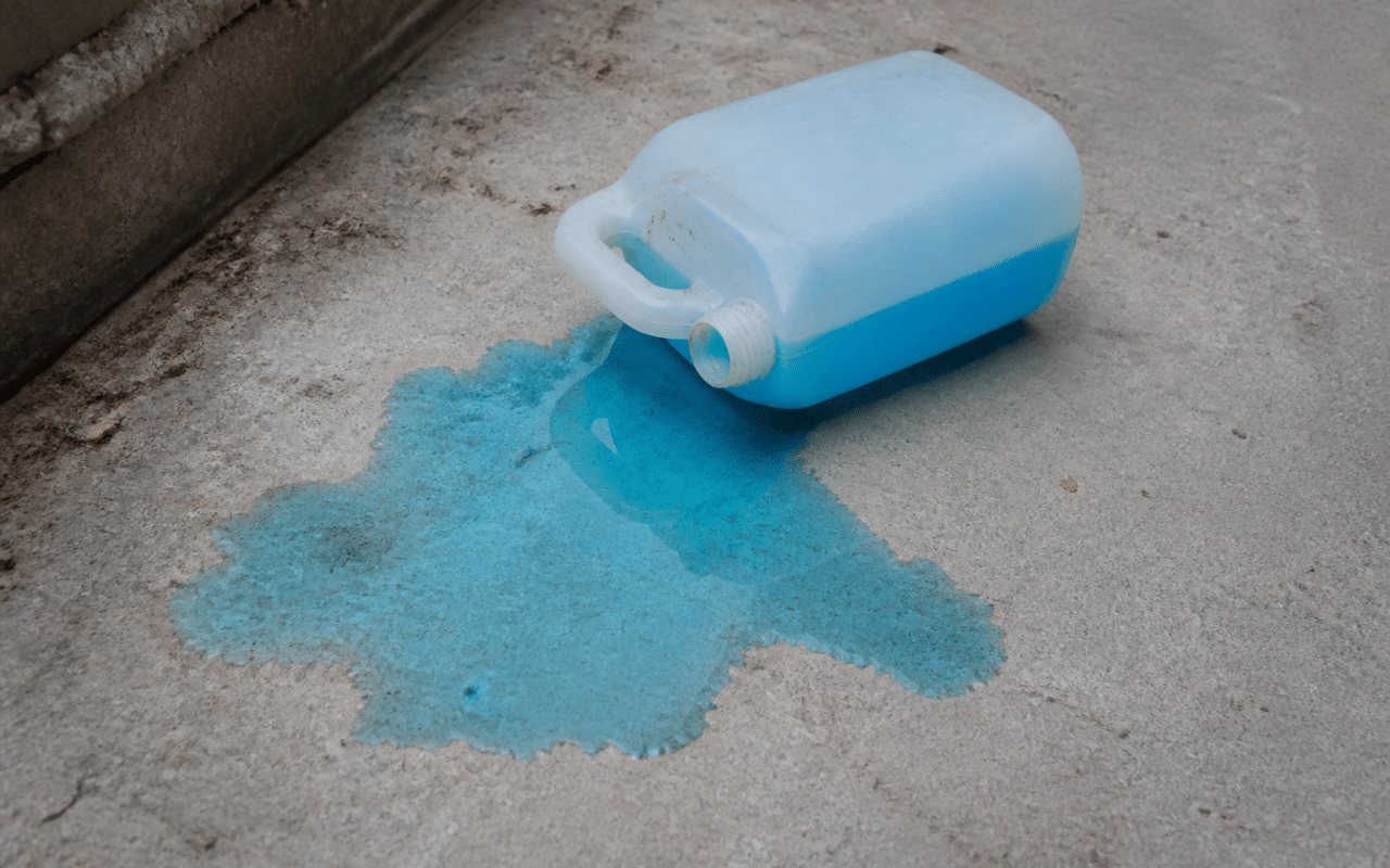 Bidon antigel bleu renverse sur sol beton gris