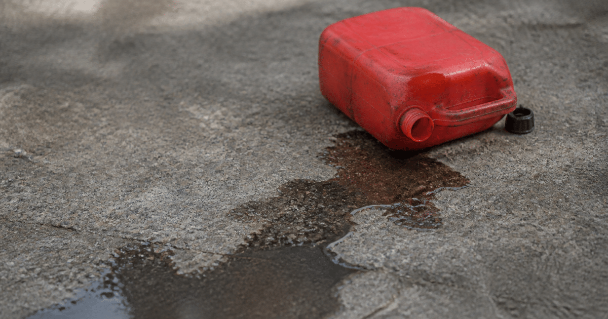 Bidon d'essence renverse sur sol gris avec liquide s'ecoulant
