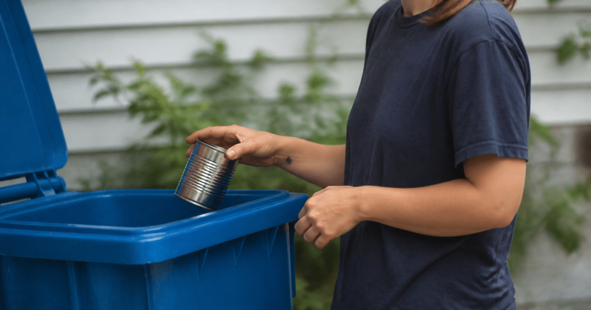 Main deposant une boite metallique dans bac recyclage bleu