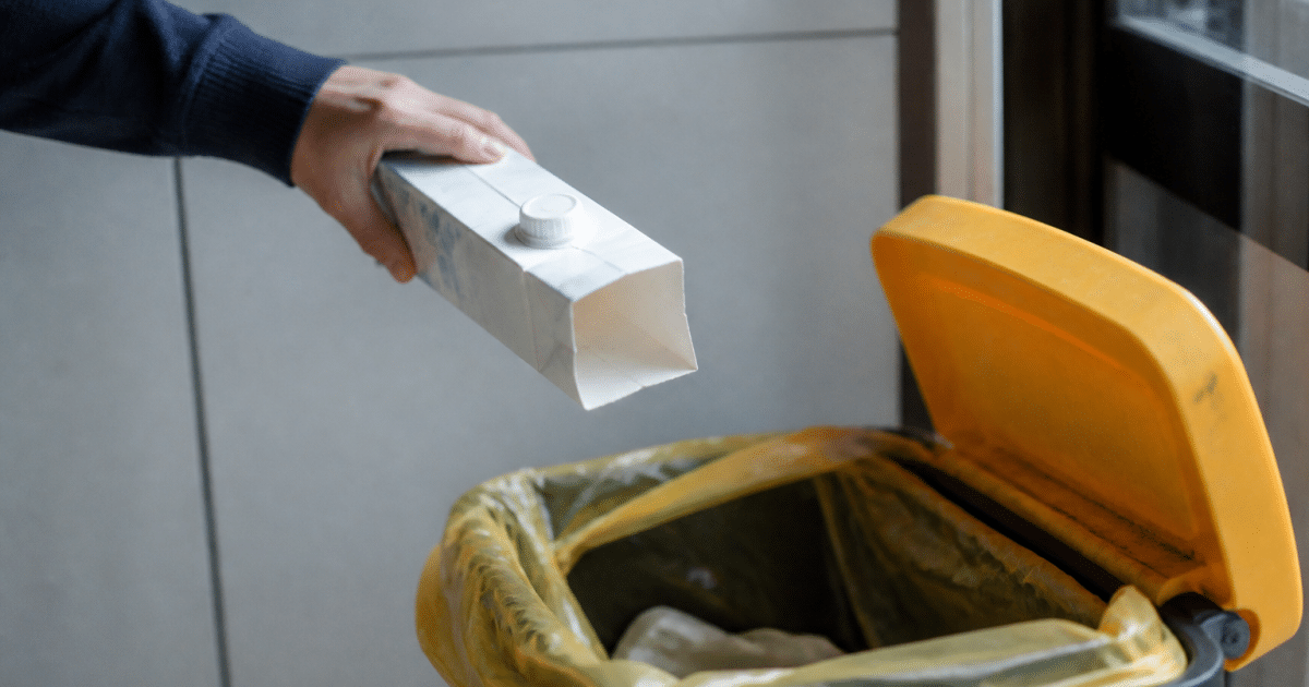 Main versant une brique de lait vide dans poubelle de recyclage