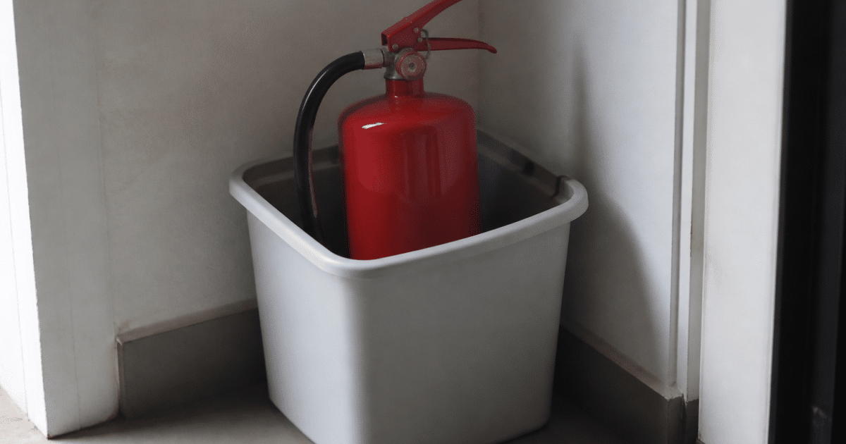 Extincteur rouge posé verticalement dans bac recycling gris