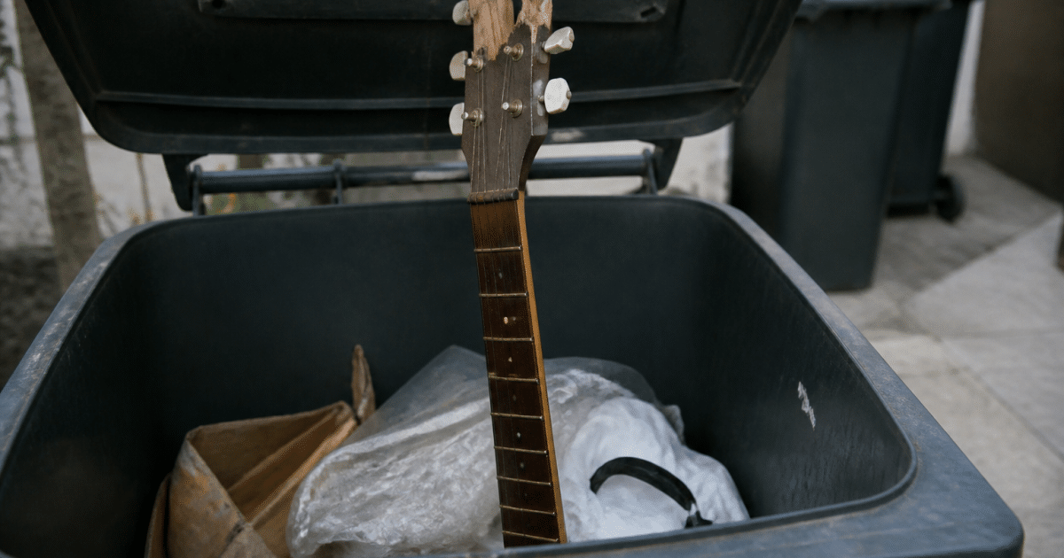 Guitare cassee posee verticalement dans benne poubelle