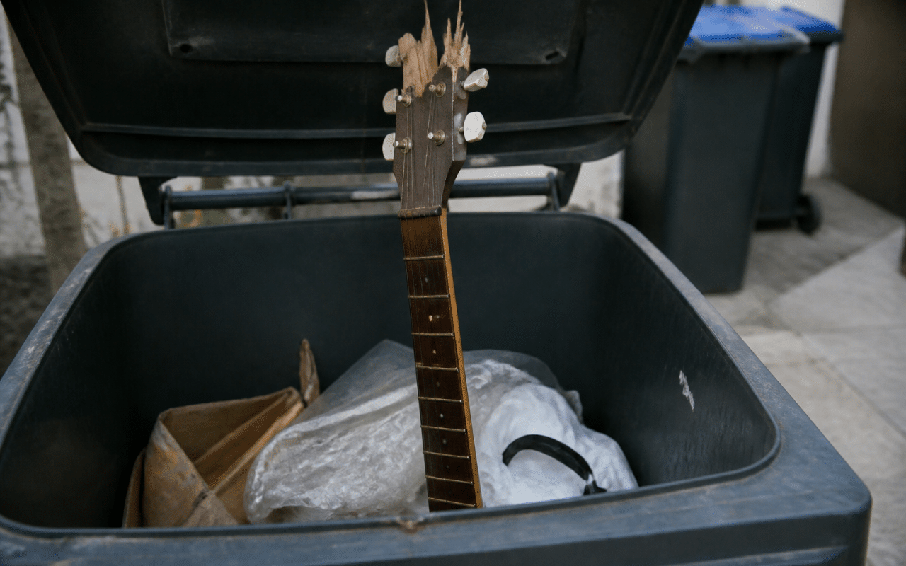Guitare cassee posee verticalement dans benne poubelle