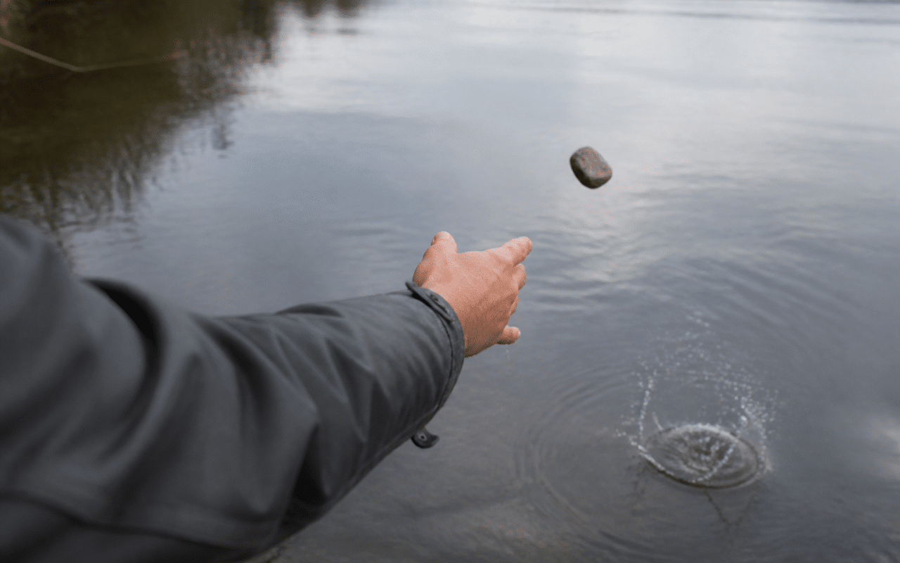 Main lancant des pierres grises dans l'eau calme