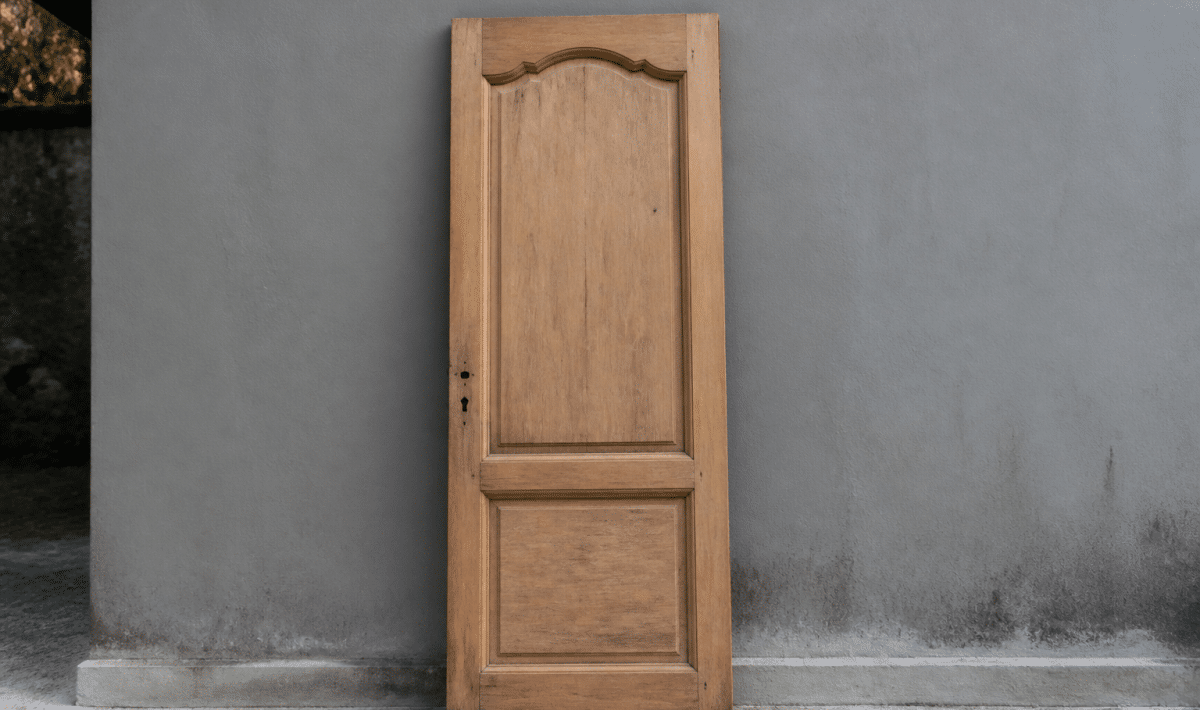 Porte en bois posee verticalement contre mur gris