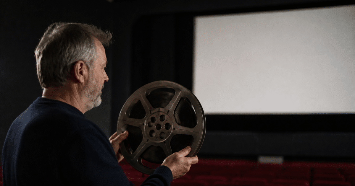 Projectioniste tenant bobine film devant ecran cinema noir