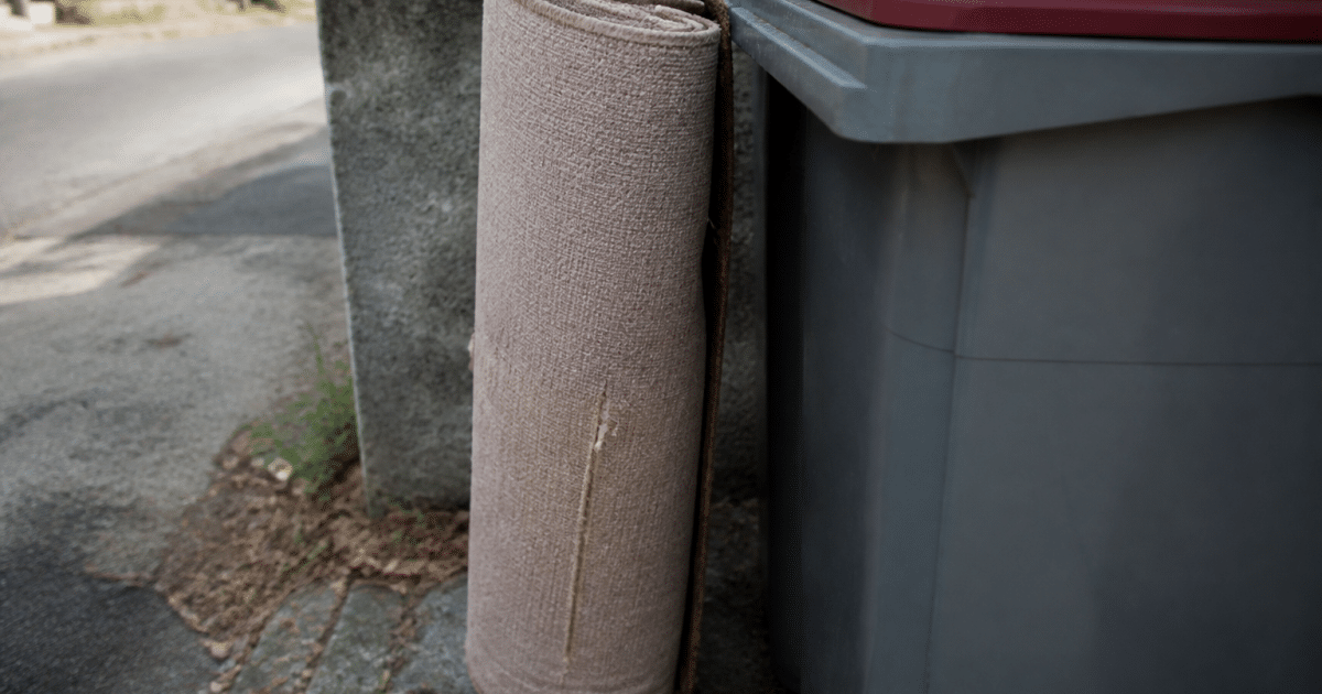 Rouleau moquette usee pose verticalement contre conteneur dechets