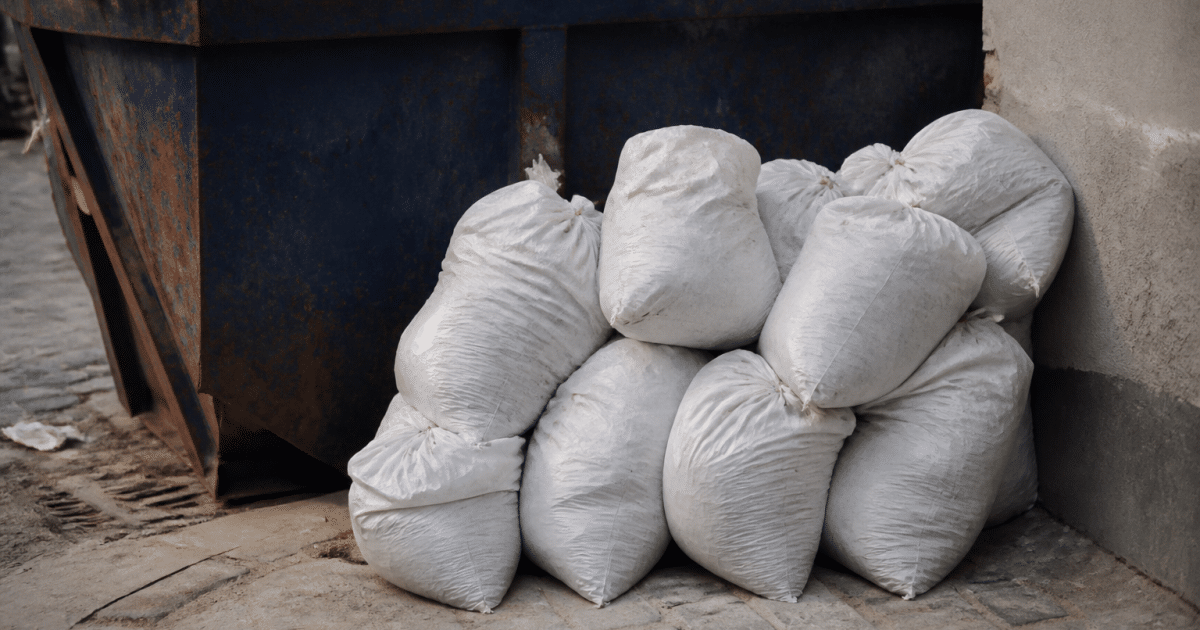Sacs de plâtre empilés près d'une benne à déchets