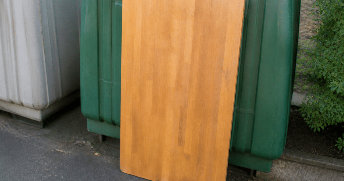 Table en bois posee verticalement contre container recyclage
