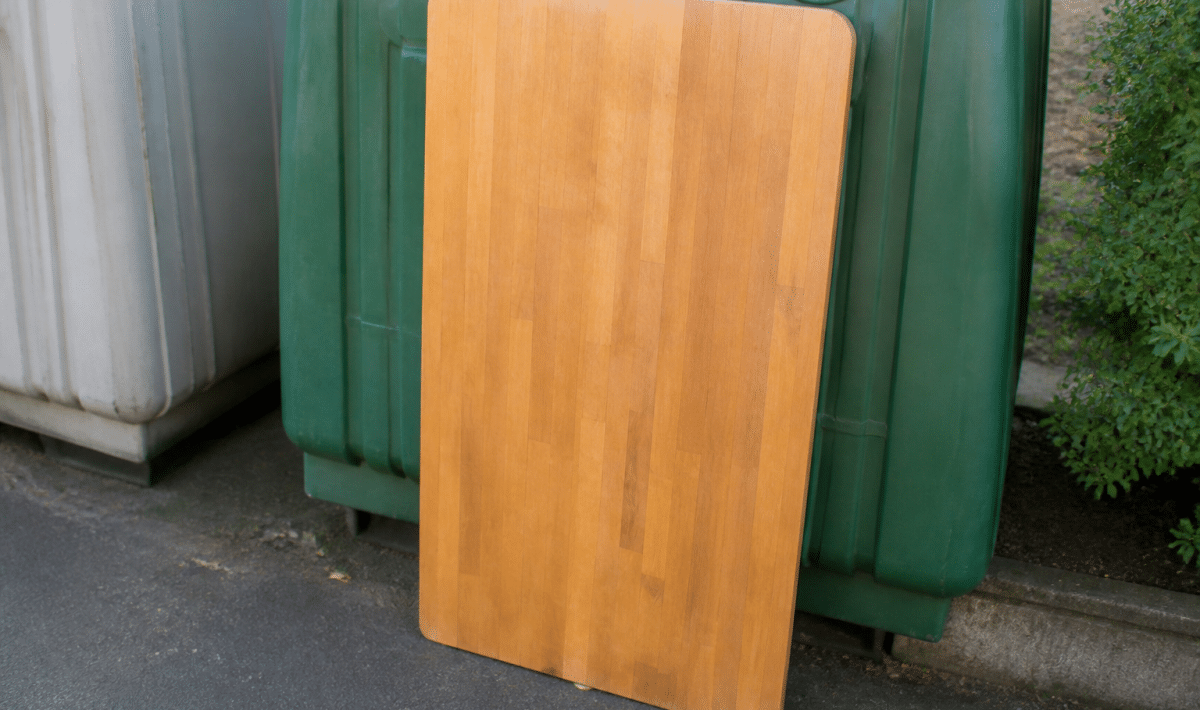 Table en bois posee verticalement contre container recyclage