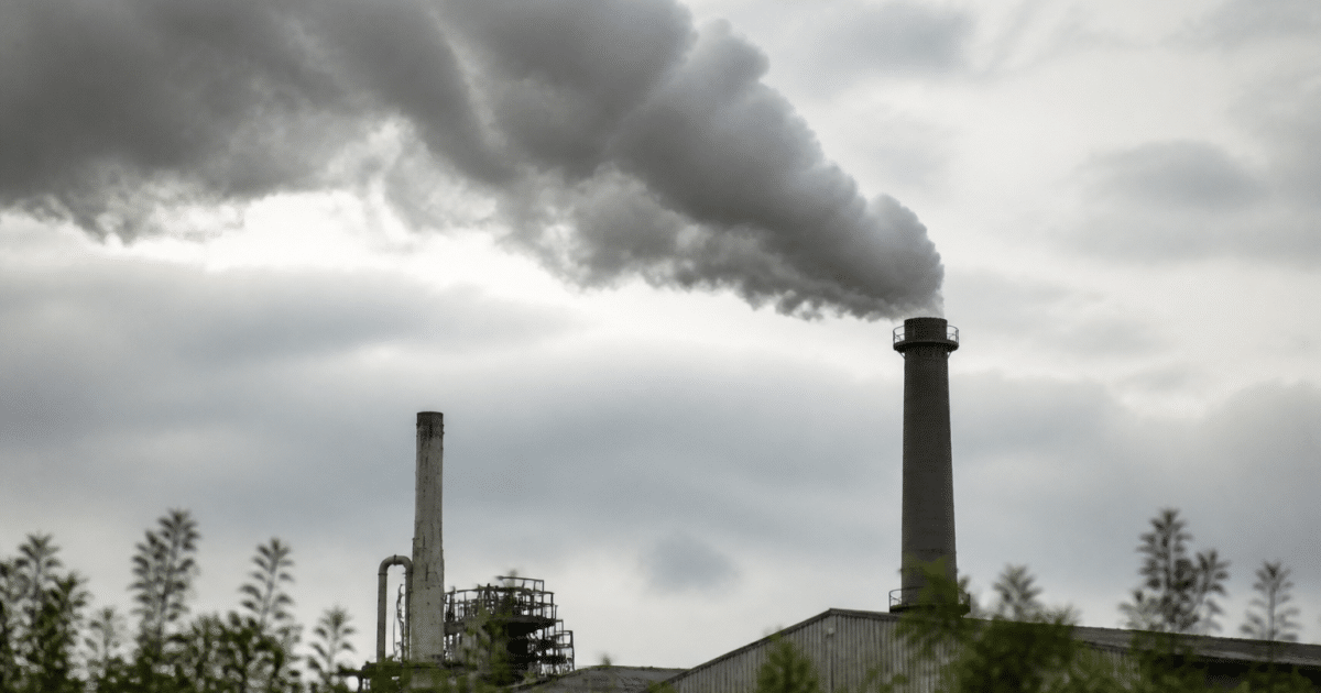 Usine rejetant fumee grise vers ciel nuageux surplombant