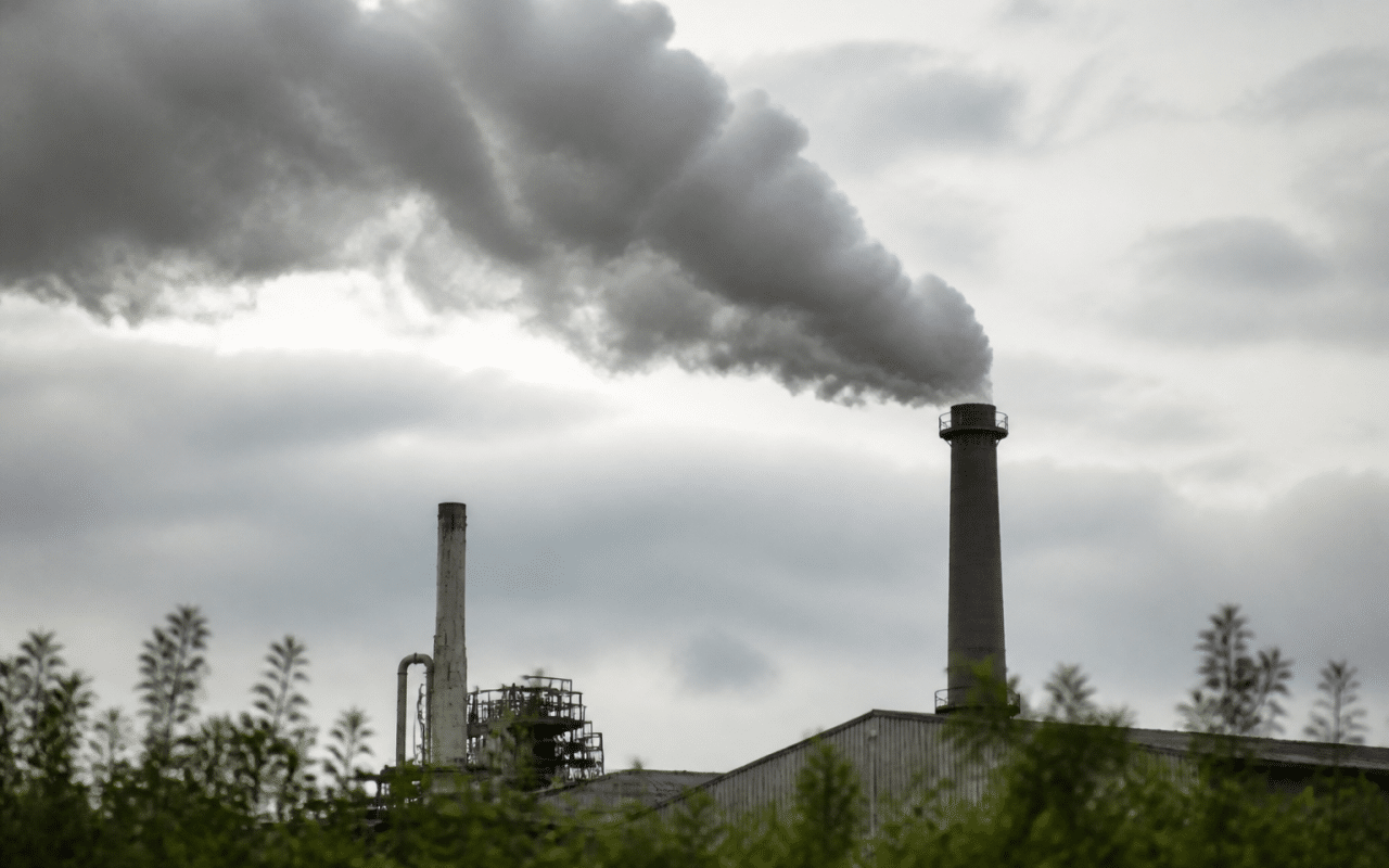 Usine rejetant fumee grise vers ciel nuageux surplombant