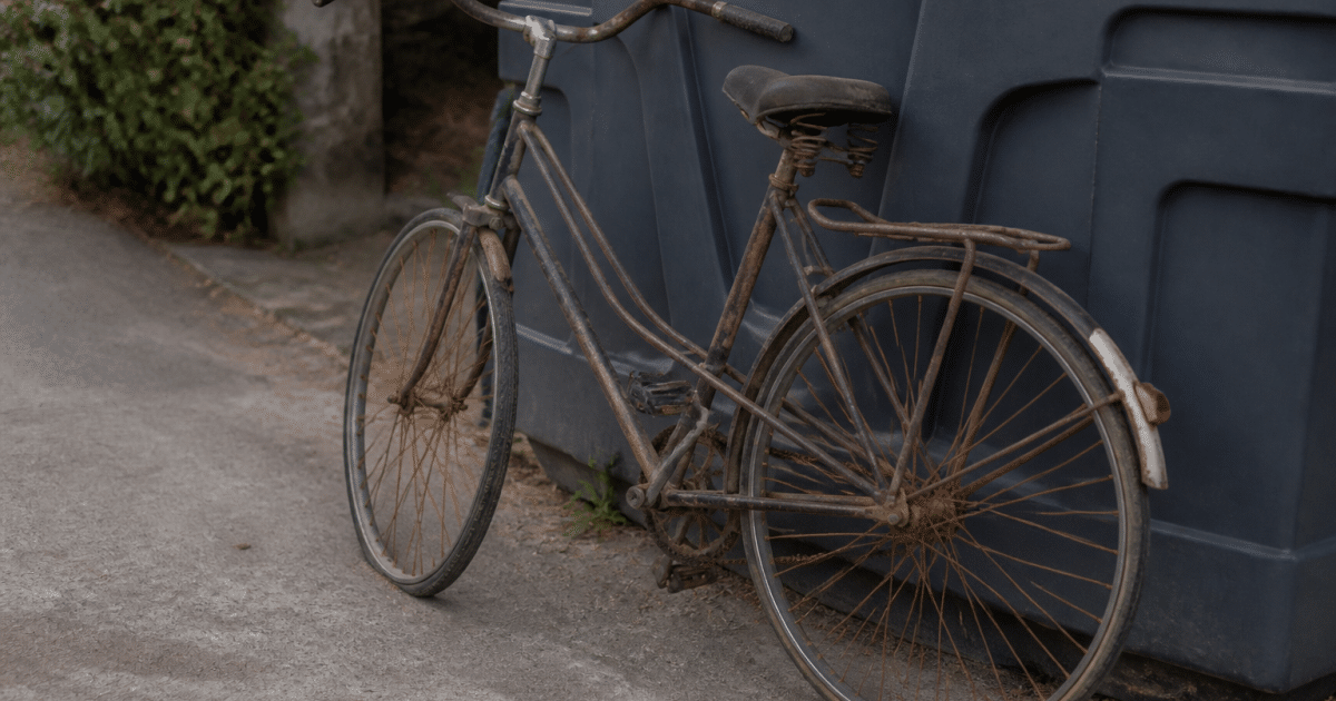 Vieux velo rouille appuye contre conteneur de recyclage exterieur
