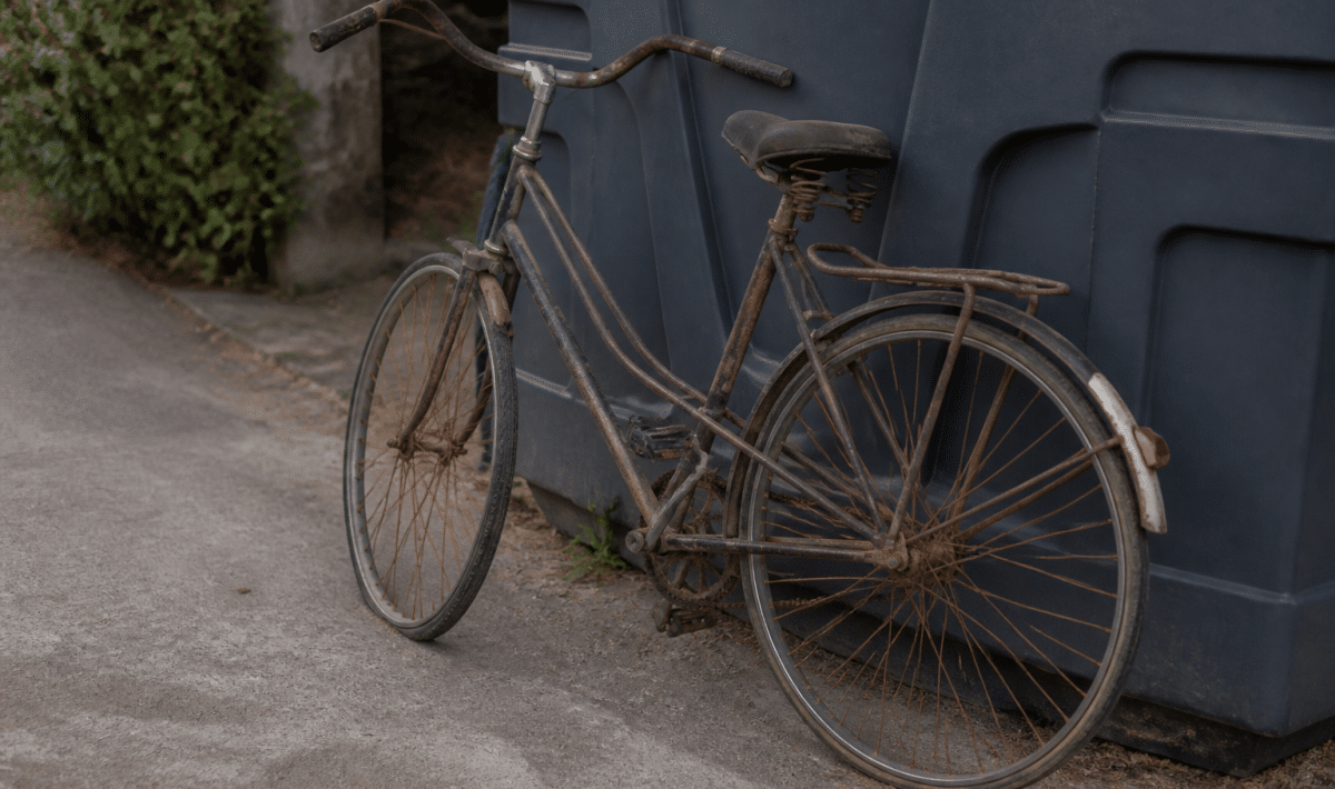 Vieux velo rouille appuye contre conteneur de recyclage exterieur