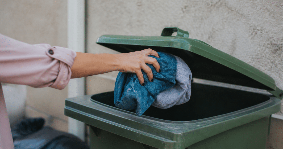 Main jetant des vetements usages dans une poubelle