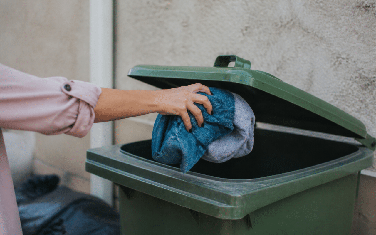 Main jetant des vetements usages dans une poubelle